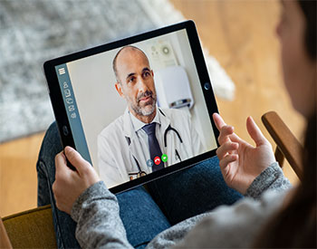 Back view of woman making video call with her doctor while staying at home.